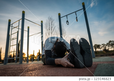 young athletic man exercising at fitness calisthenics workout and stretching legs and back at street gym during sunset, body improvement and strength training concept young athletic man exercising at fitness calisthenics workout and stretching legs and back at street gym during sunset, body improvement and strength training concept 123146823