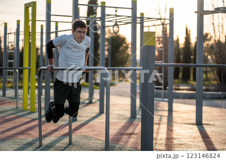 young athletic man exercising fitness calisthenics workout and making dips at street gym during sunset for body improvement and strength training 123146824