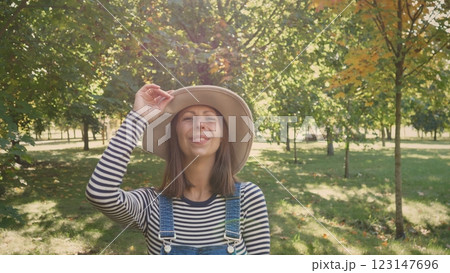 A cheerful young woman with a bright smile poses playfully in a beautifully sunlit park filled with vibrant trees 123147696
