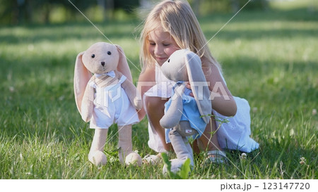 In a bright and sunny outdoor setting, a young girl joyfully interacts with her adorable plush bunny dolls In a bright and sunny outdoor setting, a young girl joyfully interacts with her adorable plush bunny dolls 123147720