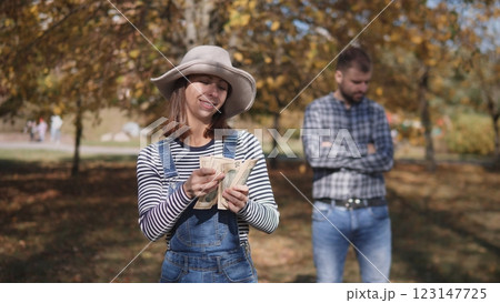 In an autumn park filled with colorful leaves, a smiling woman joyfully holds cash while a man stands behind her 123147725