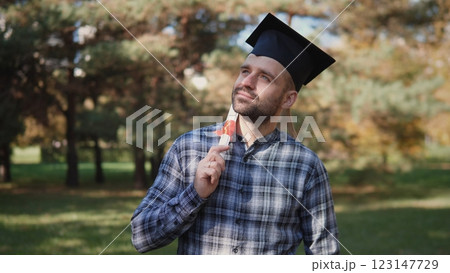 A joyful graduate wearing a cap is deep in thought about his future while surrounded by stunning autumn scenery 123147729
