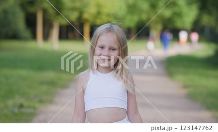 A joyful little girl smiles brightly while walking happily in a serene and peaceful park setting filled with greenery 123147762
