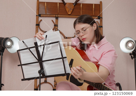 Woman with guitar flips through sheet music on music stand before starting to play acoustic guitar 123150069