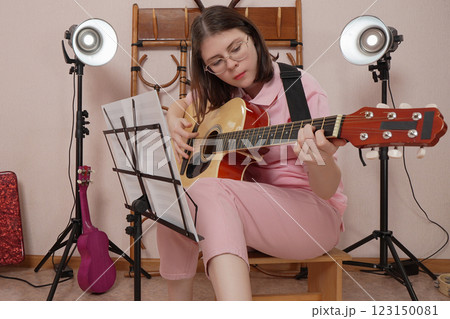Young woman practicing skill of playing acoustic guitar with strumming style in home music studio Young woman practicing skill of playing acoustic guitar with strumming style in home music studio 123150081