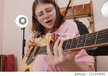 Young woman playing classical six string acoustic guitar and singing song and shaking head to beat 123150085