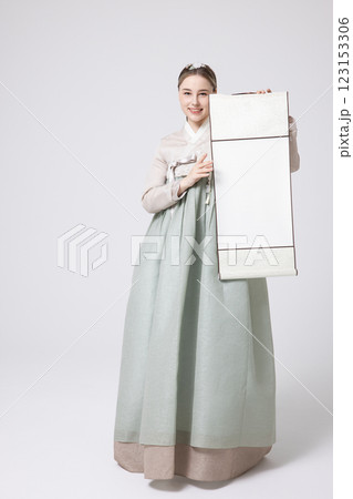 A Western woman standing wearing a Hanbok and holding a hanging scroll 123153306
