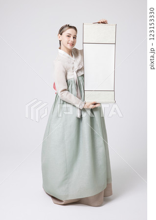 A Western woman standing wearing a Hanbok and holding a hanging scroll A Western woman standing wearing a Hanbok and holding a hanging scroll 123153330