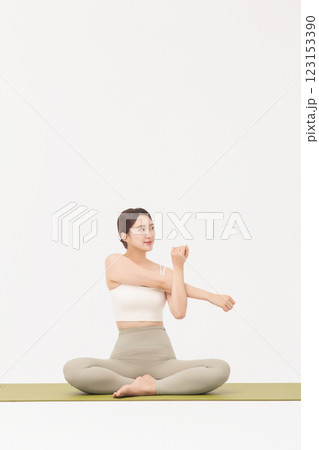 Portrait of a young woman wearing sportswear sitting on a yoga mat and stretching Portrait of a young woman wearing sportswear sitting on a yoga mat and stretching 123153390