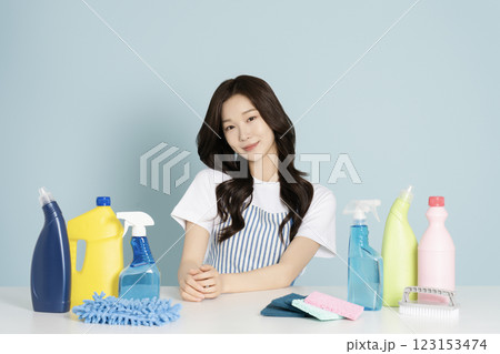A woman in her 20s sitting in an apron in front of a table with cleaning tools on it 123153474