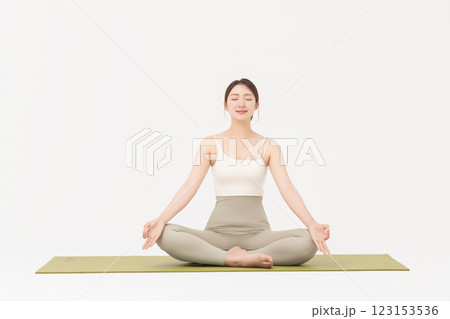 Portrait of a young woman wearing sportswear sitting on a yoga mat and stretching 123153536