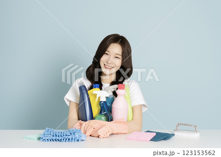 A woman in her 20s sitting in front of a table, wearing rubber gloves and holding a cleaning tool 123153562