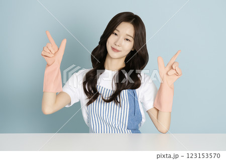 A woman in her 20s sitting in front of a table wearing rubber gloves 123153570
