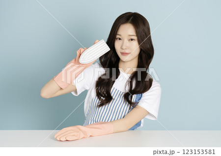 A woman in her 20s sitting in front of a table wearing rubber gloves and wiping the desk 123153581