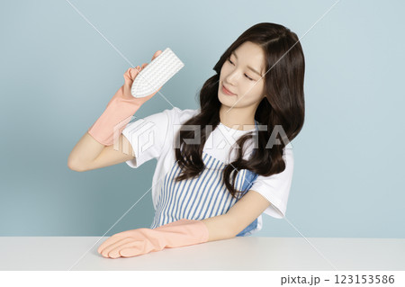 A woman in her 20s sitting in front of a table wearing rubber gloves and wiping the desk 123153586