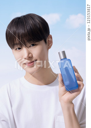 Young man holding basic cosmetics products and standing with clouds in the background Young man holding basic cosmetics products and standing with clouds in the background 123153817