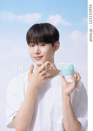 Young man holding basic cosmetics products and standing with clouds in the background Young man holding basic cosmetics products and standing with clouds in the background 123153954