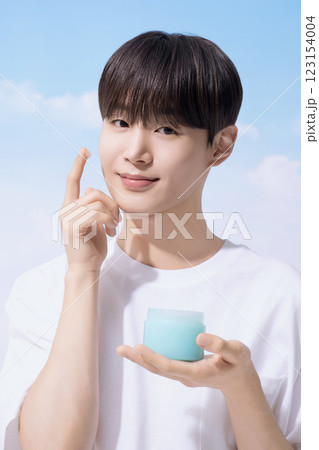 Young man holding basic cosmetics products and standing with clouds in the background Young man holding basic cosmetics products and standing with clouds in the background 123154004