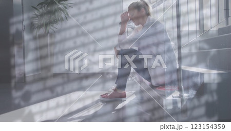 Image of rain on window over unhappy caucasian female doctor sitting on stairs in hospital 123154359