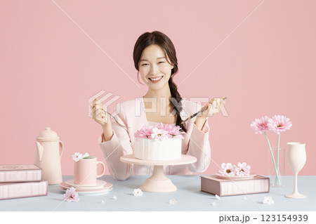 A woman in her 20s sitting in front of a cake holding a fork and knife A woman in her 20s sitting in front of a cake holding a fork and knife 123154939