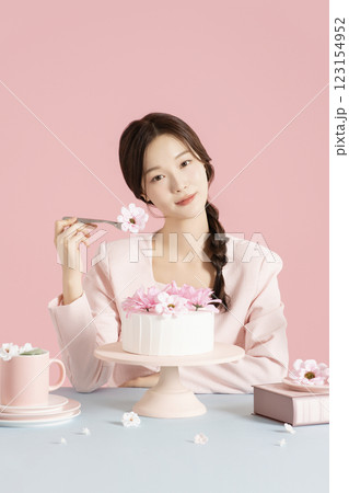 A woman in her 20s sitting in front of a cake and scooping up flowers with a fork. A woman in her 20s sitting in front of a cake and scooping up flowers with a fork. 123154952