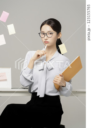 An employee in his 20s sitting in front of an office desk and a wall with post-it notes attached to it. 123155765