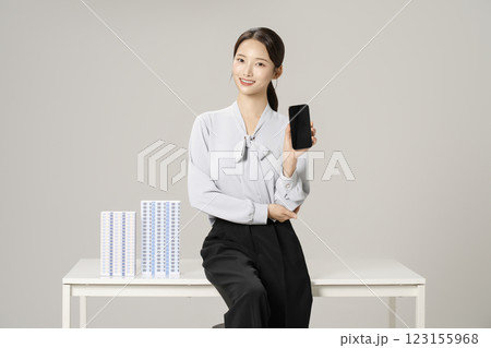 A young woman in her 20s sitting with a smartphone at a table with an apartment model on it. A young woman in her 20s sitting with a smartphone at a table with an apartment model on it. 123155968