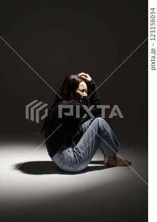A woman squatting in a lighted area 123156034