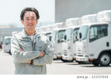 物流センターの駐車場に並ぶトラックの前にいる作業服姿の腕組みする男性（配送業・運送業・宅配業） 123157038