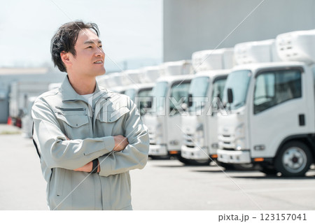 物流センターの駐車場に並ぶトラックの前にいる作業服姿の腕組みする男性（配送業・運送業・宅配業） 123157041