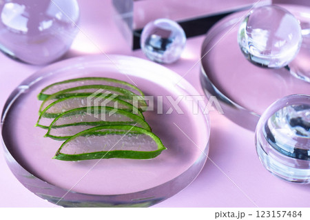 Aloe slices are arranged on a glass dish, featuring translucent spheres and a calm backdrop. 123157484