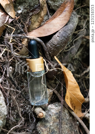 A clear serum bottle resting on roots surrounded by dried leaves and natural textures. A clear serum bottle resting on roots surrounded by dried leaves and natural textures. 123158353