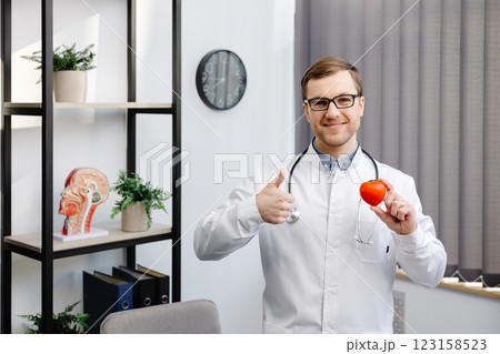 Doctor in white coat and glasses holding a red heart at hospital office. Medical health care and doctor staff service concept Doctor in white coat and glasses holding a red heart at hospital office. Medical health care and doctor staff service concept 123158523
