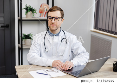 Young attractive otolaryngologist doctor sitting at his workplace in the office and holding a nose mirror 123158535