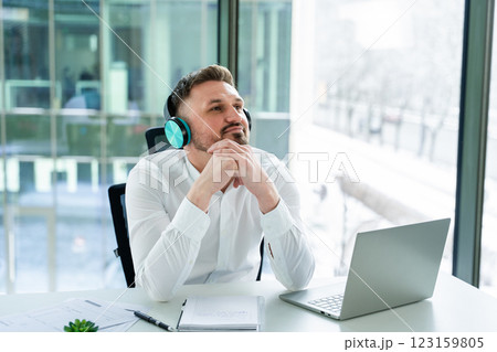 Professional Man Relaxing at Office Desk Listening to Music on Headphones 123159805