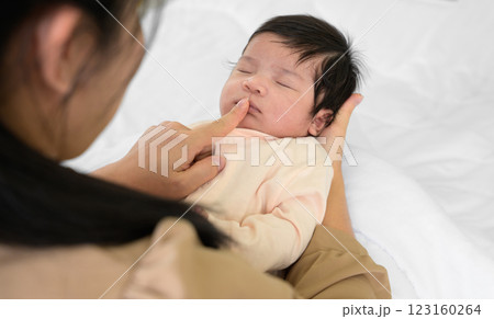 Mother touching mouth of newborn baby daughter on bed at home. Infant girl sleeping on mom arm. Love and new life concept 123160264
