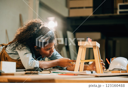 African American carpenter woman works on a wooden project using a laptop. utilize modern technology for designing new furniture, blending craftsmanship with digital tools, National Carpenters Day 123160488