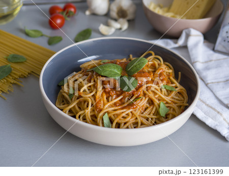 Balanesi pasta drizzled with rich tomato sauce, topped with fresh basil, nestled in sleek ceramic bowl alongside raw ingredients and kitchen tools, highlighting rustic cooking process 123161399