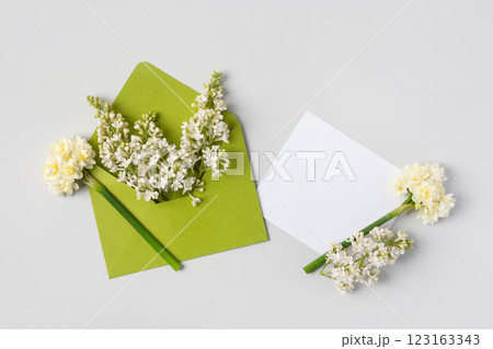 Green envelope with clean white sheet of paper for your text and spring flowers white lilac and white daffodils on gray background. Invitation to the holidays. Flat lay. 123163343