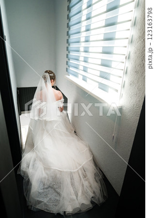 Bride in wedding gown ascending stairs, sunlight streaming through window behind. 123163798