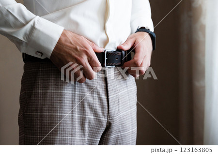 Man adjusting his belt, dressed in a white shirt and checkered trousers. 123163805