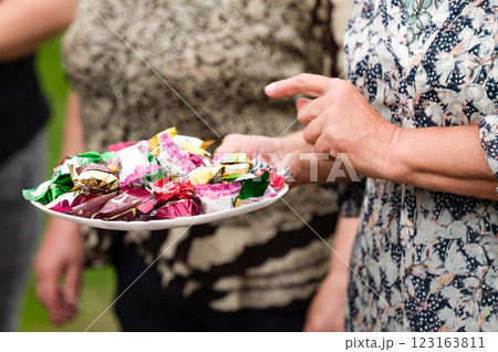 Woman offering a plate of assorted candies outdoors. 123163811