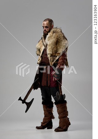 Medieval Viking warrior dressed in armor, with massive axe, showing fierce determination against grey studio background. 123163904