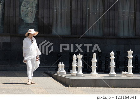 Elegant figure strolls through urban chess garden under the midday sun with unique giant pieces 123164641
