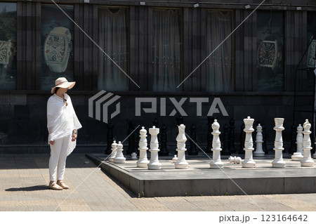 Elegant woman contemplating a giant chess game in a historic urban setting during a sunny afternoon Elegant woman contemplating a giant chess game in a historic urban setting during a sunny afternoon 123164642