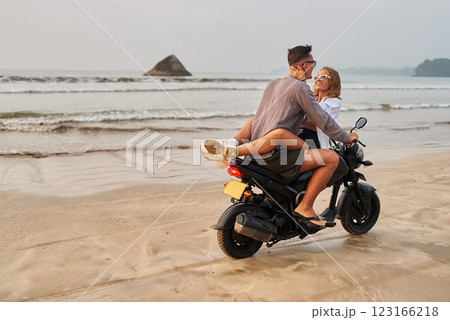 Young couple on beach motorbike. Lovers enjoy sand, sea riding motorcycle. Girl hugs guy on scooter, explore ocean shore romance, adventure. Man, woman on bike holiday. 123166218