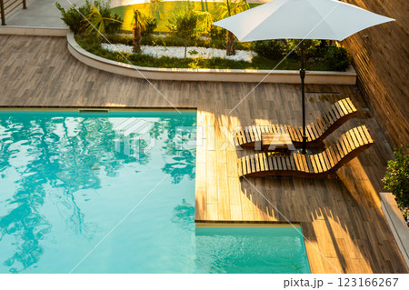 Elegant poolside wooden deck with curved lounge chairs, umbrella, and turquoise pool in a tranquil backyard Elegant poolside wooden deck with curved lounge chairs, umbrella, and turquoise pool in a tranquil backyard 123166267