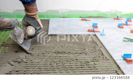 Tiler at work applies cement glue to the floor to install tiles. Construction. 123166588