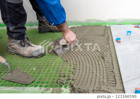 Tiler at work applies cement glue to the floor to install tiles. Construction. 123166590
