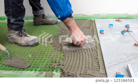 Tiler at work applies cement glue to the floor to install tiles. Construction. 123166591